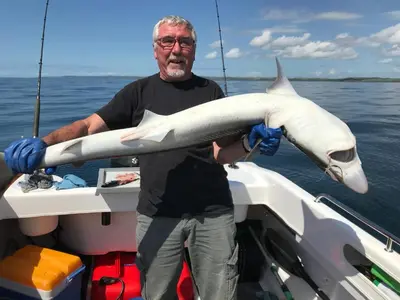 a man holding a shark in a boat at Curlew Cottage and Sunset View in Port Logan