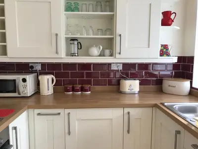 a kitchen with white cabinets and red tile on the wall at Curlew Cottage and Sunset View in Port Logan