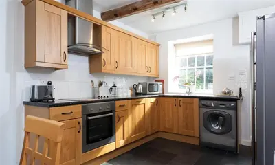 a kitchen with wooden cabinets and a washer and dryer at Pollys Cottage in Elterwater