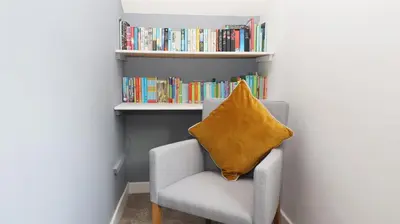 a chair with a yellow pillow in front of a book shelf at Bowderstone in Keswick