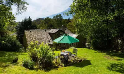 a woman sitting in a chair under a green umbrella at Underheron in Grasmere