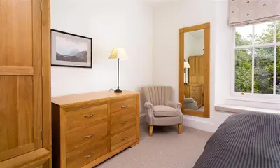 a bedroom with a dresser and a chair and a mirror at Ben House in Grasmere