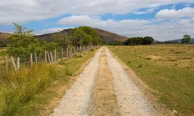 a dirt road in a field next to a fence at Scalegill House in Cockermouth