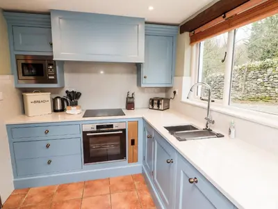 a kitchen with blue cabinets and a sink and a window at Gunpowder Cottage in Elterwater