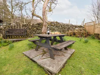 a picnic table in a yard with a stone wall at Gunpowder Cottage in Elterwater