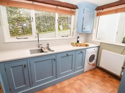 a kitchen with blue cabinets and a washing machine at Gunpowder Cottage in Elterwater