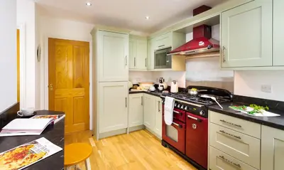 a kitchen with white cabinets and a red stove top oven at Artists Hideaway in Portinscale