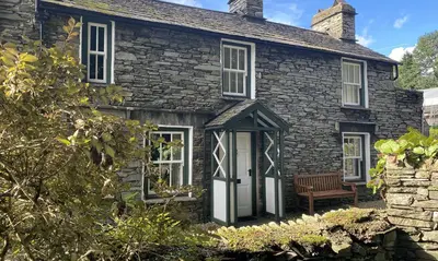 a stone house with a bench in front of it at Dove Holme Cottage in Grasmere