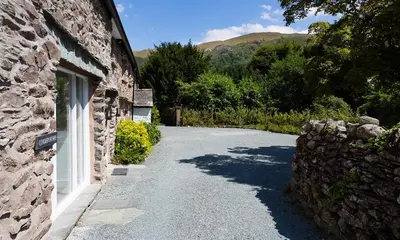 a stone building with a driveway next to a stone wall at Underhowe in Grasmere