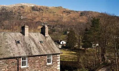 an old brick house with a mountain in the background at High Raise in Grasmere