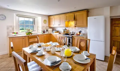 a kitchen with a wooden table with chairs and a white refrigerator at Low Longthwaite Farm in Watermillock