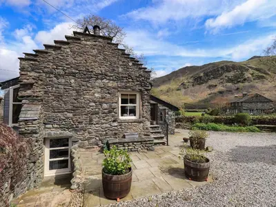 a stone house with a bench and mountains in the background at Beckside Studio in Patterdale