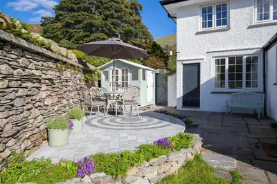 a patio with a table and an umbrella in front of a house at Crozier Cottage in Ambleside