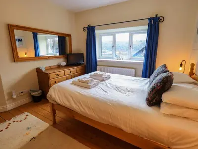 a bedroom with a bed with blue curtains and a window at Daisy Cottage in Grasmere