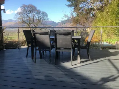 a table and chairs on a deck with mountains in the background at Dancing Beck Cottage in Keswick