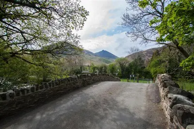 a dirt road with a stone wall and mountains at Grisedale Cottage in Keswick