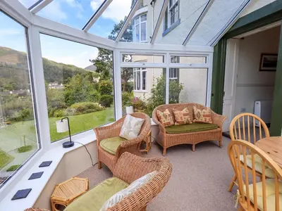 a conservatory with chairs and a table and windows at Sandburne Cottage in Keswick