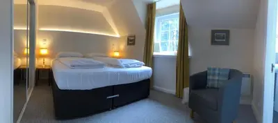 a bedroom with a large bed and a chair at Lategillan Cottage in Polmood