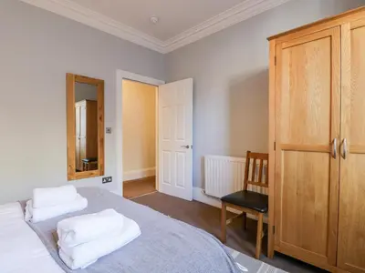 a bedroom with a bed and a chair and a mirror at Carlton House Apartment 1 in Keswick