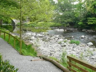 a wooden bench next to a river with a bridge at Keswick Bridge 13, within walking distance of Keswick town centre, strictly no pets in Keswick