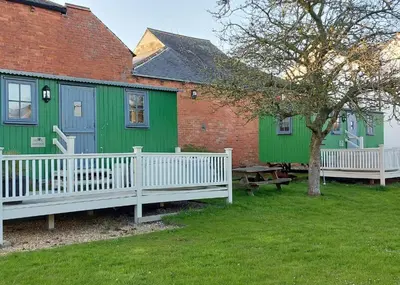 a group of green and blue buildings with a picnic table at Ryans Retreat, Bowness on Solway perfect for a break when walking Hadrians Wall with a hot tub in Bowness-on-Solway