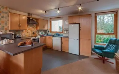a kitchen with wooden cabinets and a blue chair at Keswick Bridge 10, within walking distance of Keswick town centre, strictly no pets in Keswick