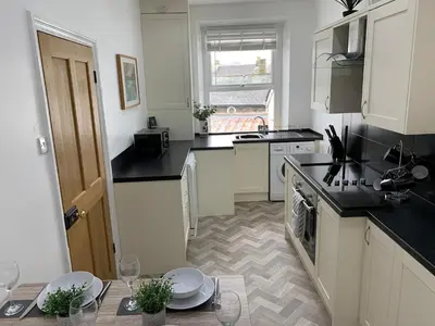 a kitchen with white cabinets and a table with wine glasses at Ridge View - Amazing Roof Terrace in Keswick