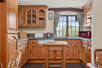a kitchen with wooden cabinets and a table at The Mountain Cottages - Carpenters in Coniston