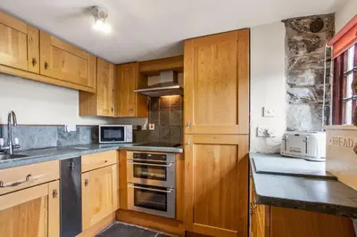 a kitchen with wooden cabinets and a stove top oven at The Mountain Cottages - Sawyers in Coniston