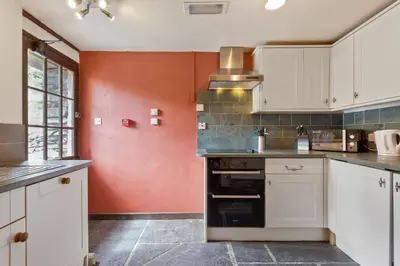 a kitchen with white cabinets and a red wall at The Mountain Cottages - Pelton Wheel in Coniston