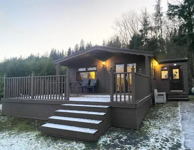 a small cabin with a porch and a deck at 4 Bed House - Sleeps 9 - HotTub - Parking in Beattock