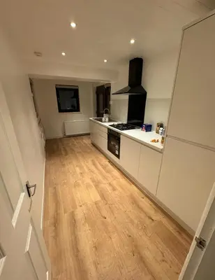 a kitchen with white cabinets and a wooden floor at 4 Bed House - Sleeps 9 - HotTub - Parking in Beattock