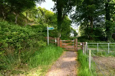 a fence next to a dirt road with a gate at Garden Cottage in Stranraer