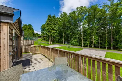 a patio with a table and chairs on a wooden deck at Squirrel Lodge 42 with Hot Tub in Newton Stewart