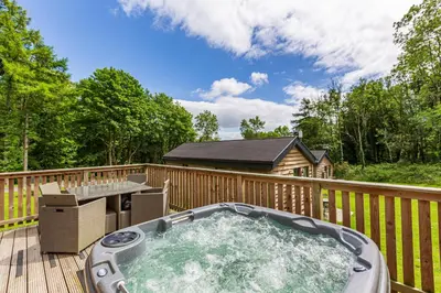 a hot tub on a wooden deck with a table at Squirrel Lodge 42 with Hot Tub in Newton Stewart
