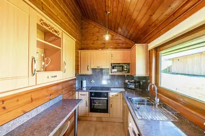 a kitchen with wooden cabinets and a sink and a window at Lady Galloway 27 with Hot Tub in Newton Stewart