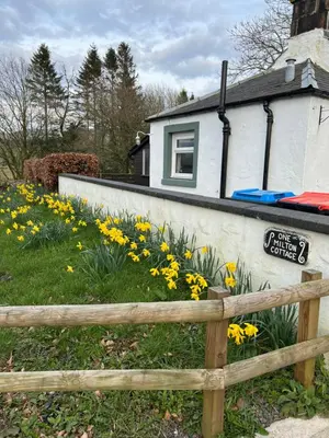 a fence in front of a house with yellow flowers at Cosy country cottage in rural location in Moffat