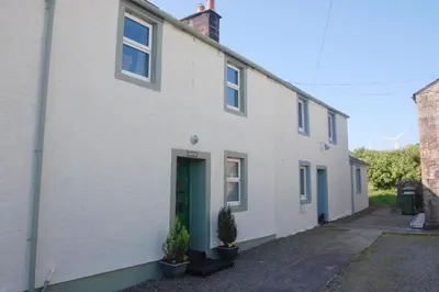 a white house with a green door and two potted plants at Pinfold Cottage on the edge of lake district in Bothel