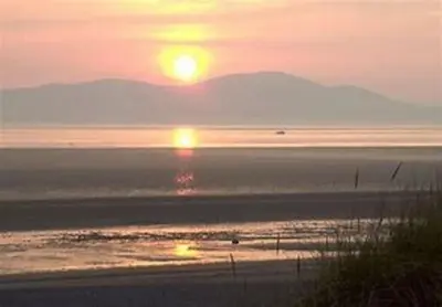 a sunset over a beach with the sun setting at Pinfold Cottage on the edge of lake district in Bothel
