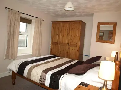 a bedroom with a bed and a wooden cabinet at Pinfold Cottage on the edge of lake district in Bothel