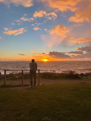 a man standing next to a fence watching the sunset at Immaculate 2-Bed Static Caravan at Monrieth in Newton Stewart