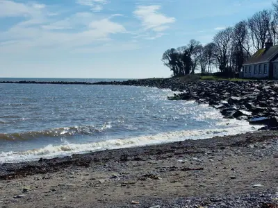 a rocky shoreline with a house and the water at Stunning Caravan Whithorn3 in Newton Stewart