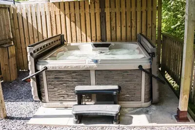 a hot tub with a stool and a chair in front of a fence at Reflections, Netherby, a micro cabin with hot tub in a rural setting in Longtown