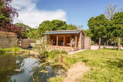 a wooden cabin with a pond in the yard at The Chard, Netherby, a micro cabin in a rural setting with a hot tub in Longtown