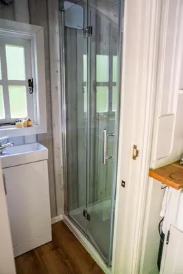 a glass shower in a bathroom with a sink at The Snug, Netherby, cute shepherds hut with hot tub in a rural location in Longtown