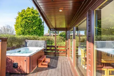 a hot tub on a deck next to a house at Birch Lodge 12 with Hot Tub in Newton Stewart