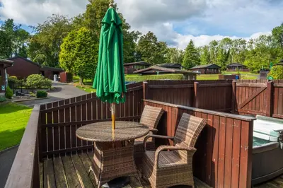 a table with a green umbrella on a deck at Bluebell Lodge 5 with Hot Tub in Newton Stewart