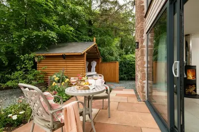 a patio with a table and a dog house at Daisy Cottage, Dalston, peaceful, rural setting with garden & hot tub in Carlisle