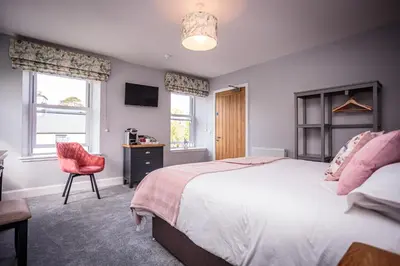 a bedroom with a bed and a chair and windows at The Kenmuir Arms Hotel in New Luce