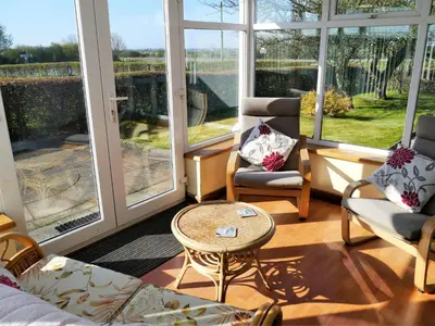 a living room filled with furniture and large windows at Woodhall Cottage in Annan